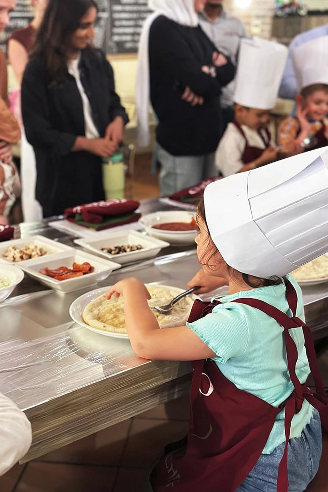 Child in chef hat making pizza